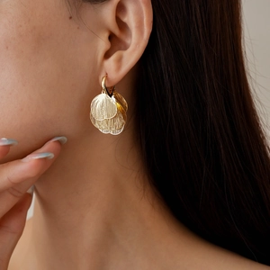 Detailed view of gold layered petal earrings with hollow texture on a female model