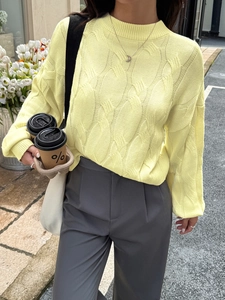 Close-up of pale yellow knit sweater featuring detailed cable knit texture and crew neck