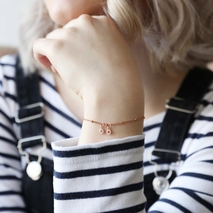 Close-up of rose gold bracelet with transparent gem and red star charm on wrist