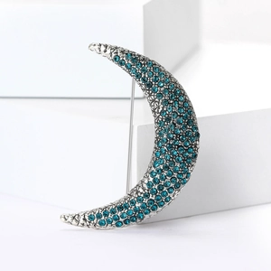 Close-up of silver crescent moon brooch with blue rhinestones on a white cube