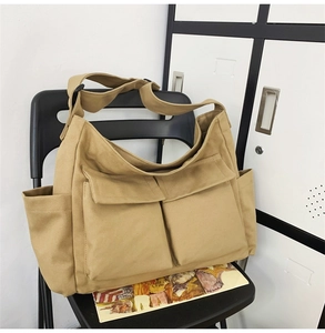 Detailed view of khaki canvas shoulder bag with dual front flap pockets on a chair