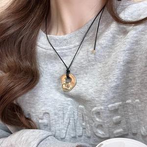 Detail of a golden fluid-shaped heart pendant on a black cord necklace worn by a model
