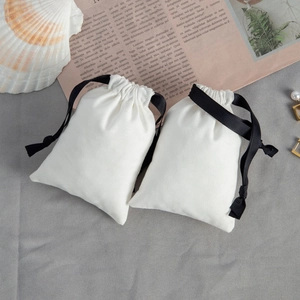 Flat lay of white cotton jewelry drawstring pouches with black ribbon on newspaper