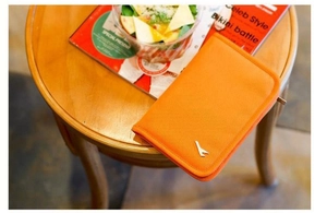 Flat lay of an orange travel passport wallet with metal logo on a rustic wooden table