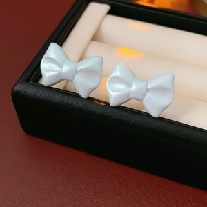 Macro detail of pearl white bow stud earrings inside a premium black jewelry box