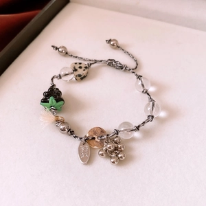 Detail of handmade beaded bracelet featuring heart stone, glass grape charm and oval tag