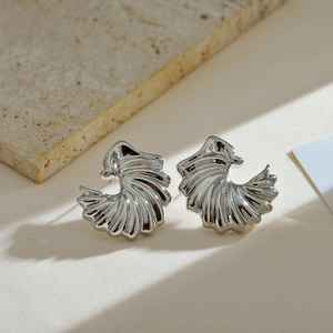 Macro detail of elegant silver seashell earrings on minimalist marble and fabric surface