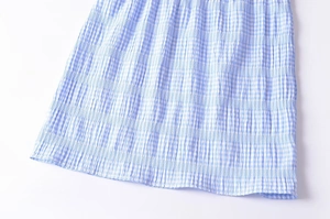 Detailed close-up of blue and white plaid fabric texture and pleated hem of the skirt