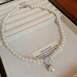 Detail of elegant pearl necklace featuring a teardrop pendant with zircon stones