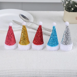 Set of mini sequin Christmas hat cutlery holders in five colors on a white tablecloth