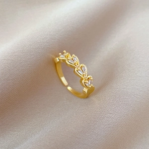 Detail of gold double-row heart ring with white zircons on champagne silk fabric