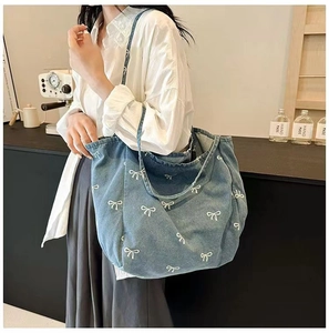 Close-up of a large denim tote bag featuring white bow prints on a model's shoulder