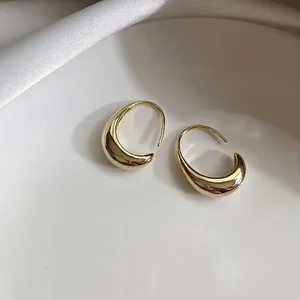 Elegant gold teardrop hoop earrings on white silk fabric inside a ceramic tray
