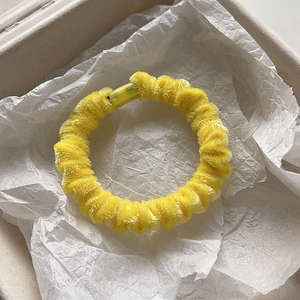 Dettaglio dell'elastico per capelli in velluto giallo con texture morbida in ciniglia