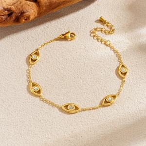 Gold evil eye bracelet with crystal charms on natural sandy background with wood decor