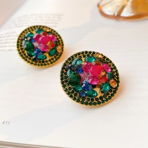 Detailed close-up of vintage round gold clip earrings with colorful rhinestones on book pages