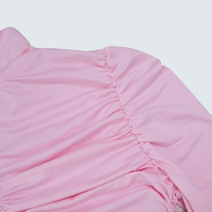 Détail d'une robe rose à manches longues avec coutures froncées aux épaules et plis doux