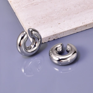 Close-up of hollow silver hollow C-shaped ear cuffs on a textured stone and mirror surface