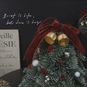 Miniature Christmas tree with red velvet bow and golden bells on a dark background