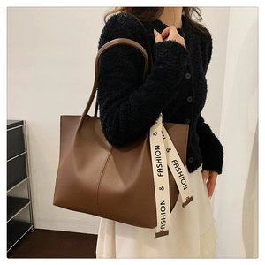 Detail of a large dark brown tote bag with fashion straps worn by a model in a business casual style