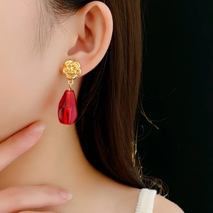 Close-up of elegant golden rose flower earrings with a red teardrop-shaped glass pendant