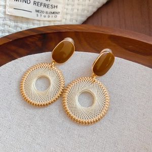 Macro detail of yellow woven geometric hoop earrings on textured linen background