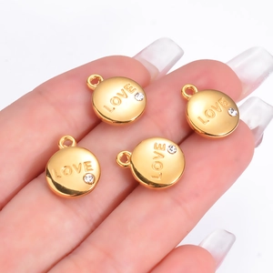 Lot de 4 pendentifs LOVE dorés avec strass présentés sur la main de face