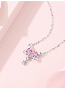 Macro detail of silver heart necklace with pink pear-cut stones and planet charm
