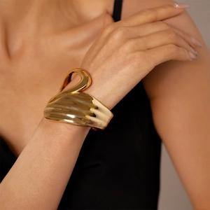 Close-up of a golden asymmetric open cuff bracelet with swan-inspired geometric curves