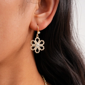 Detailed view of women wearing gold snowflake earrings with sparkling white crystals