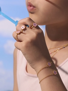 Detailopname van gouden kinderarmband en ringen met roze geëmailleerde bloembedels