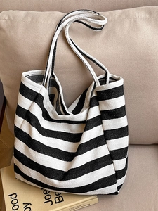 Minimalist black and white striped canvas tote bag on a beige sofa with a book