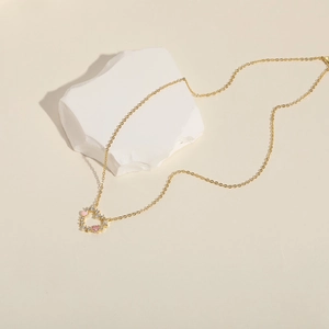 Dettaglio di una collana a cuore rosa con cristalli bianchi su catena d'oro su pietre