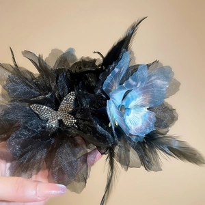 Detailed view of hair clip with blue iridescent flower, black mesh, and feather tassels