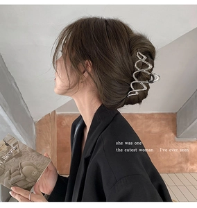 Detail view of a large silver wave-shaped metal hair claw clip worn on a low bun