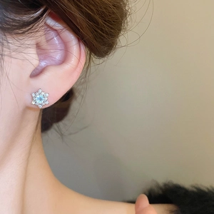 Close-up of a silver snowflake earring with light blue zircon on a model's ear