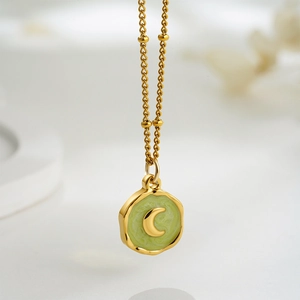 Close-up of 18K gold crescent moon pendant with light green enamel on a bead chain