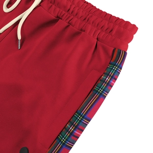 Detail of red joggers featuring white drawstring and side Scottish plaid pattern trim