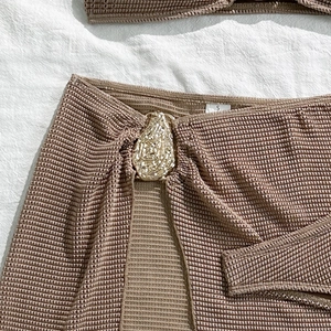 Macro detail of khaki crochet bikini skirt with wave-textured gold metal buckle, size S label