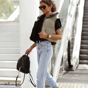 Outdoor street view of a woman wearing a light khaki short puffer vest and denim jeans
