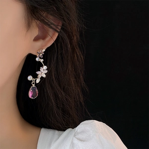 Elegant gold flower earrings with purple crystal teardrop pendants on female model