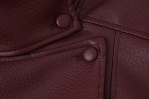 Macro shot of dark wine red PU leather jacket showing detailed stitching and fabric buttons