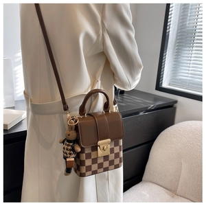 Detail of brown checkered crossbody bag with gold hardware and small bear charm