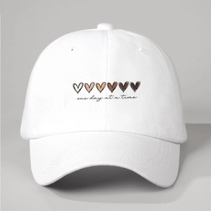 Detail of white cotton baseball cap featuring gradient hearts and cursive text embroidery