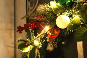 Close-up of lighted Christmas wreath with red berries, pine needles and plaid ribbon