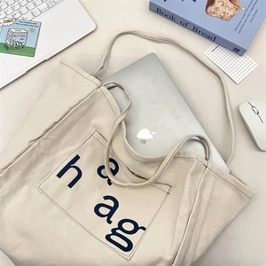 Close-up of cream canvas tote bag with side pocket holding a laptop for office use
