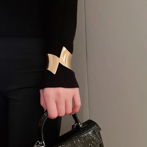 Dettaglio macro di un ampio bracciale dorato ondulato irregolare sul polso del modello