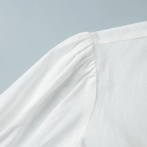 Detailed view of the pleated shoulder and natural linen texture on a white puff sleeve top