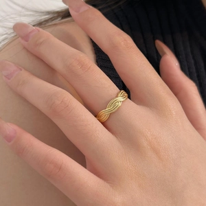Close-up of a minimalist golden braided twist ring featuring a fine woven metal texture