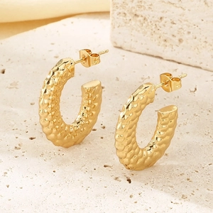 Macro detail of gold-plated C-shaped earrings with textured fish scale pattern finish